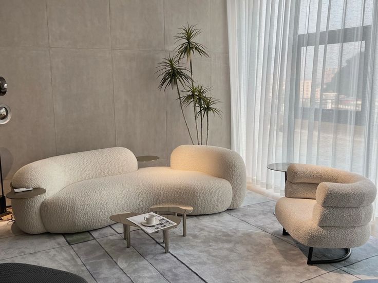 a living room filled with furniture next to a large glass window covered in white curtains