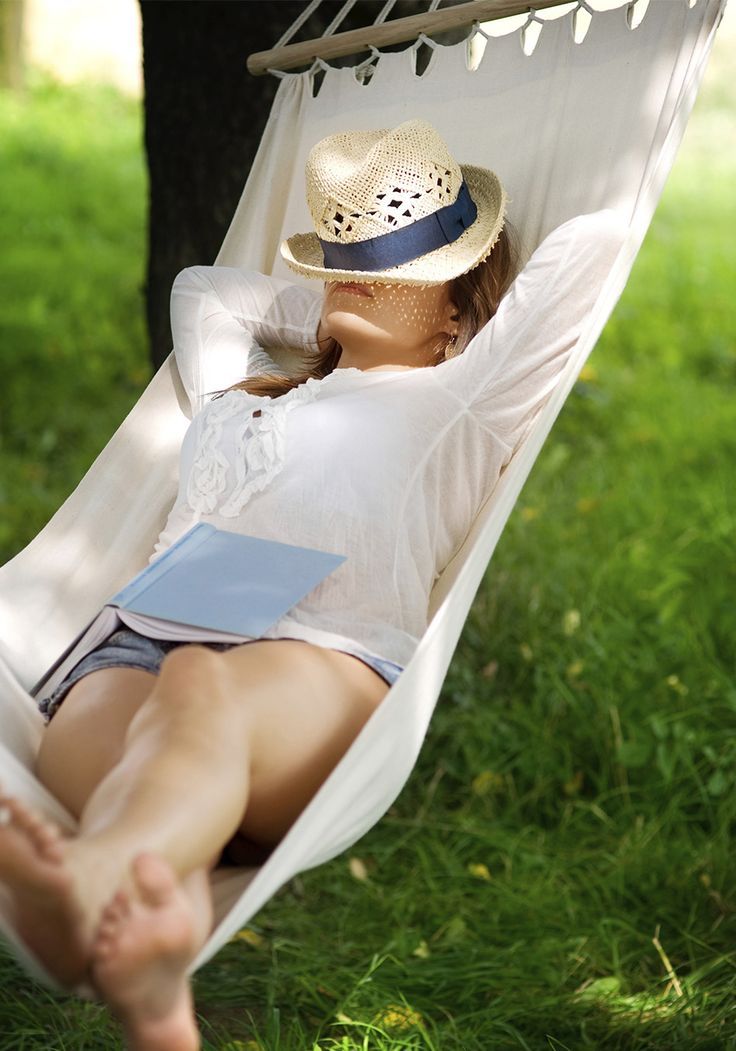 a woman laying in a hammock reading a book