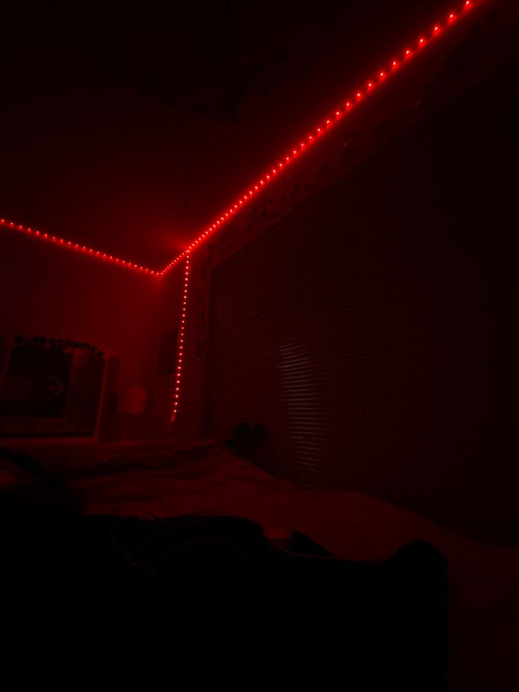 a dark room with red lights on the ceiling and bed in the foreground,