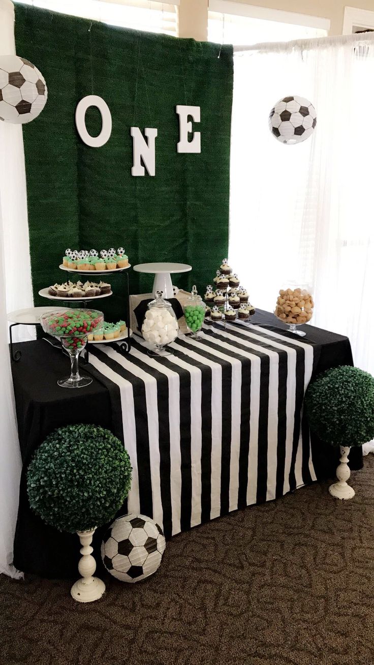 a black and white table topped with desserts and soccer ball decorations on top of a carpeted floor