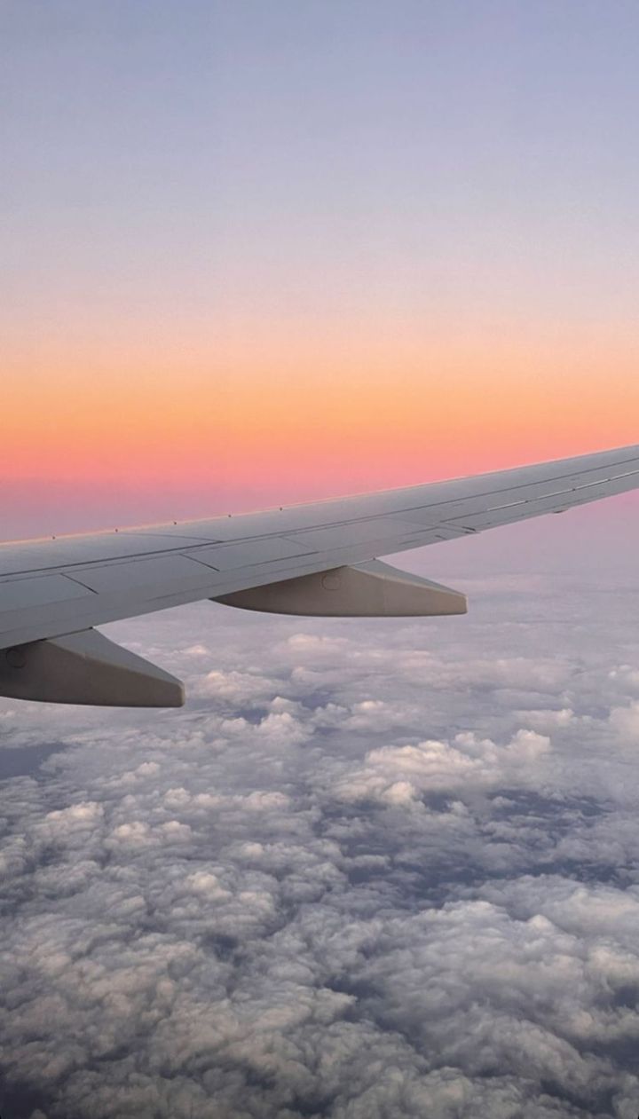 the wing of an airplane as it flies through the sky above clouds at sunset or dawn