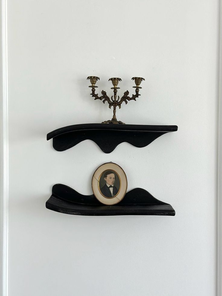 two black shelves with candles on top of each shelf and a small candle holder in the middle