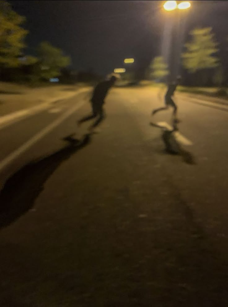 two skateboarders are riding down the street at night