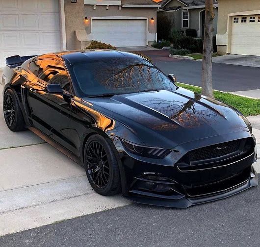 a black mustang parked in front of a house with orange flames painted on the hood