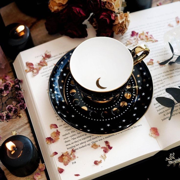 a cup and saucer sitting on top of an open book next to some flowers