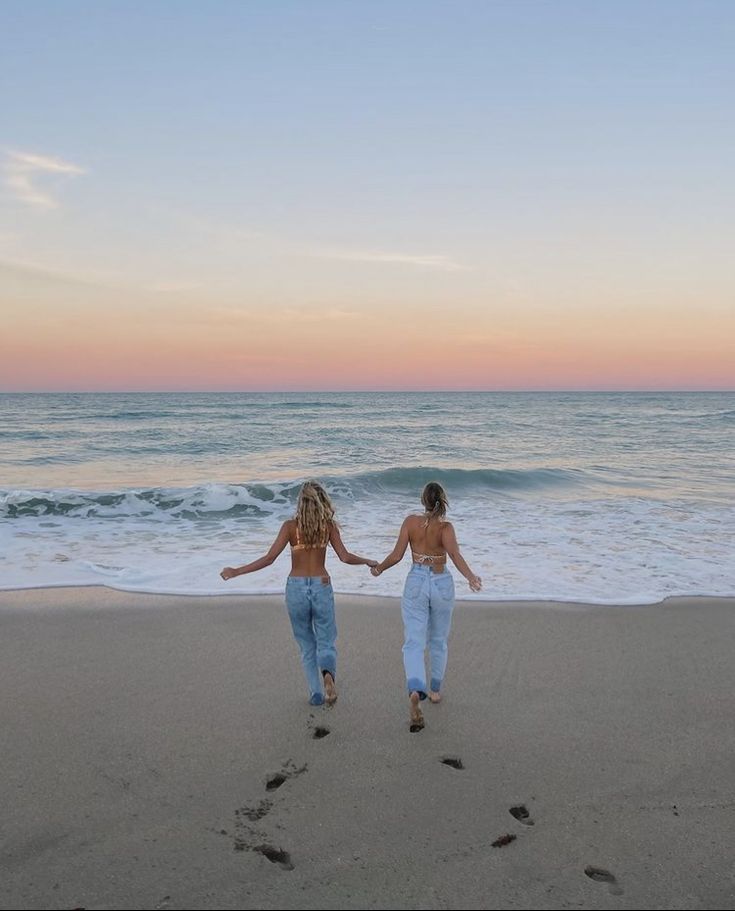 two women walking on the beach with their hands in each other's pockets as the sun sets