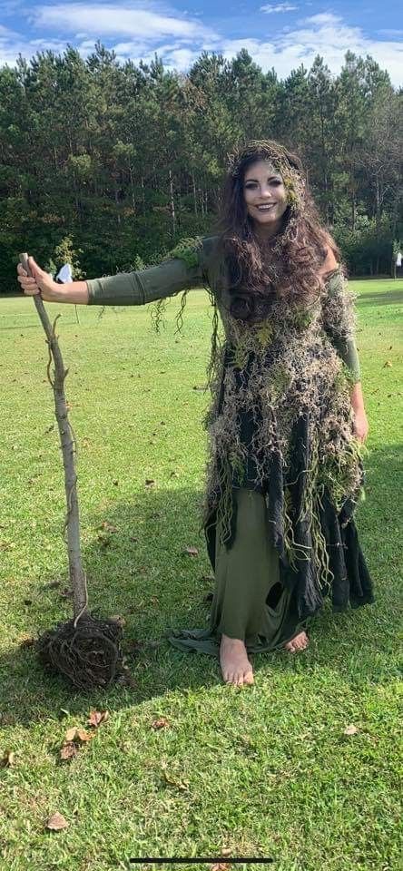 a woman with long hair is standing next to a tree and holding it in her hands