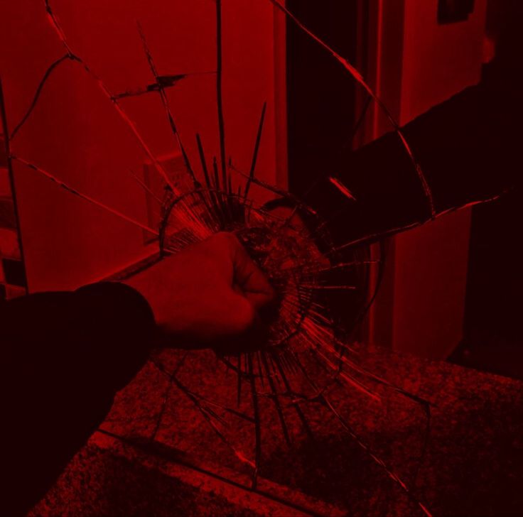 a hand holding a broken glass in front of a red wall with the light on