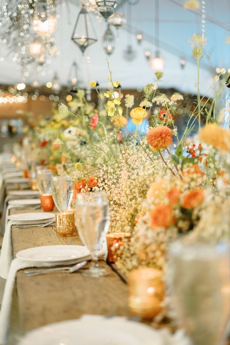 A head table at a wedding reception decorated with baby's breath down the entire 25 foot table with dahlias, ranunculus, roses, anemones, and wild flowers poking out of it. All with a color scheme of orange, peach, yellow, red, and dark purple. Designed by the florists at Camrose Hill. Camrose Hill is an outdoor wedding venue and florist located in Stillwater, Minnesota. Classy Elegant Wedding Dress, Wedding Decor Reception, Classy Elegant Wedding, Yellow Wedding Decorations, Summer Wedding Venues, Wildflower Centerpieces, Stillwater Minnesota, Yellow Wedding Theme, Dahlias Wedding