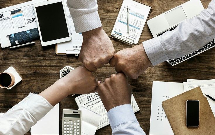 two people holding hands over a wooden table with papers and other office supplies on it