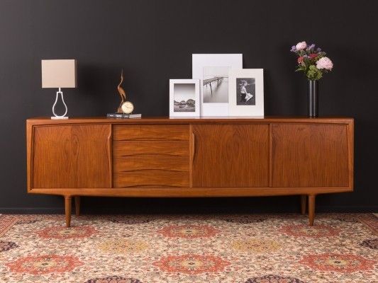 a wooden sideboard with two pictures on top and flowers in vases next to it