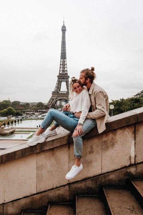 two people sitting on the edge of a wall in front of the eiffel tower