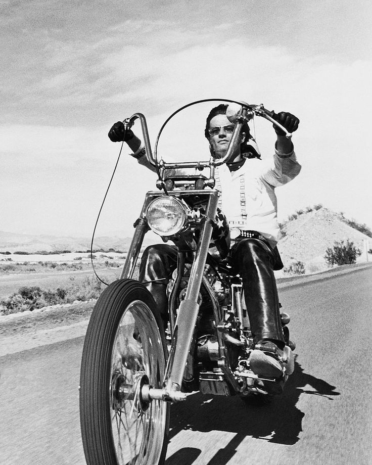 a man riding on the back of a motorcycle down a road next to a desert