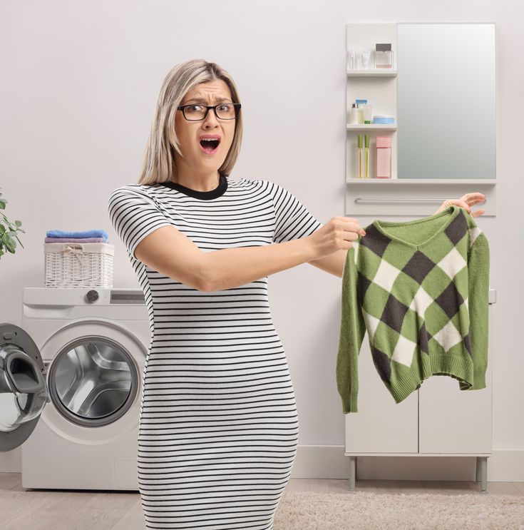 a woman holding up a green sweater in front of a washer