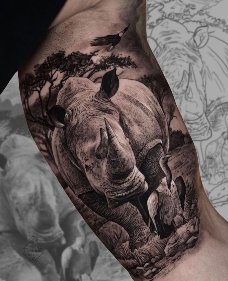 a rhino tattoo on the arm with birds and trees in the background, it is black and white