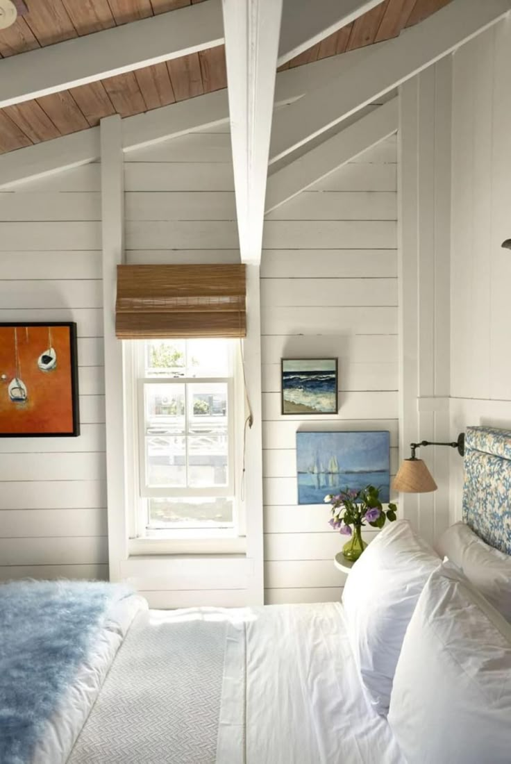 a bedroom with white walls and wood ceilinging, along with a bed covered in blue and white sheets