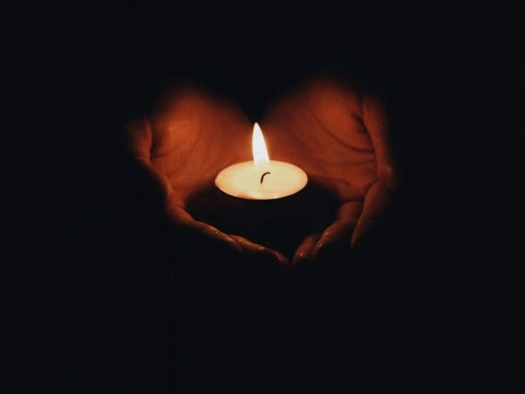 a person's hands holding a lit candle in the middle of their heart shape