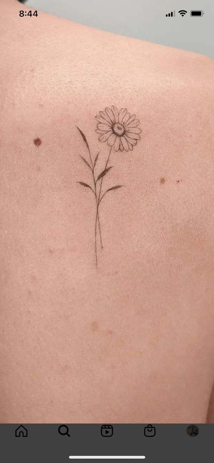 the back of a woman's shoulder with a single flower tattoo on her left side