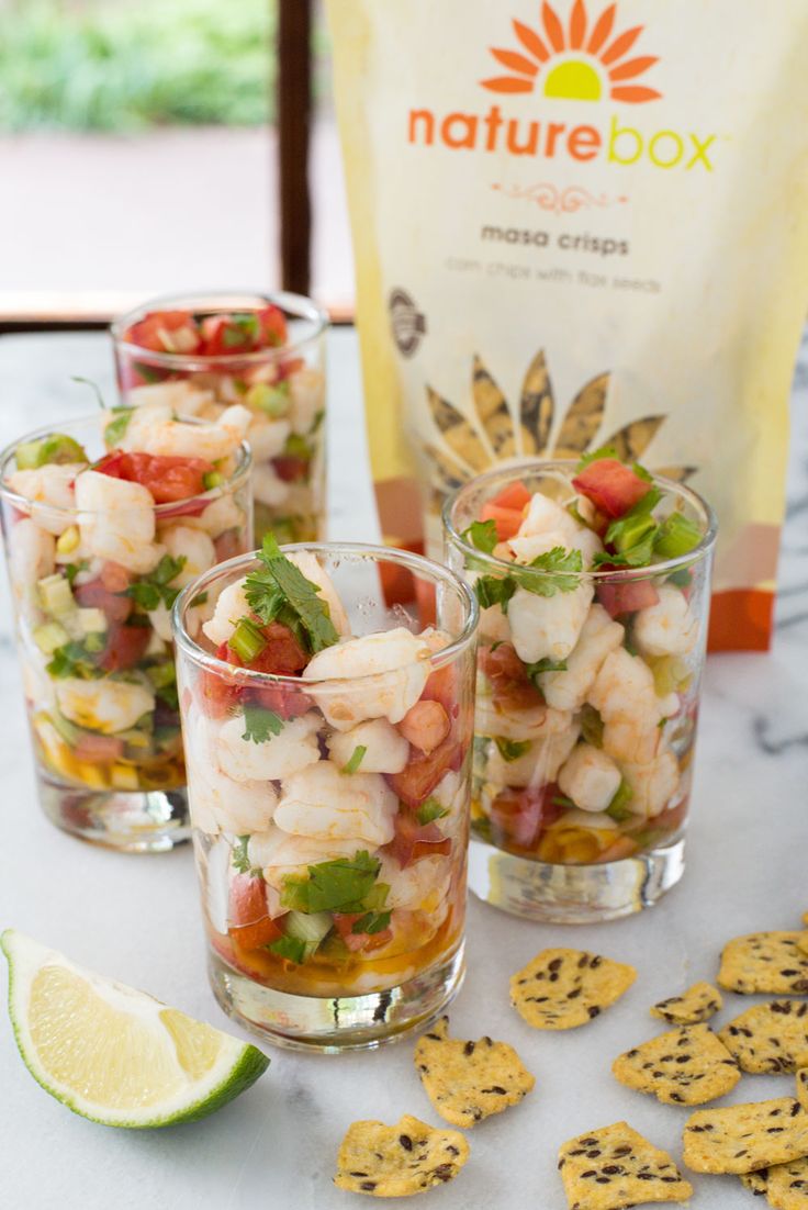 three shot glasses filled with shrimp salad next to crackers and a bag of chips