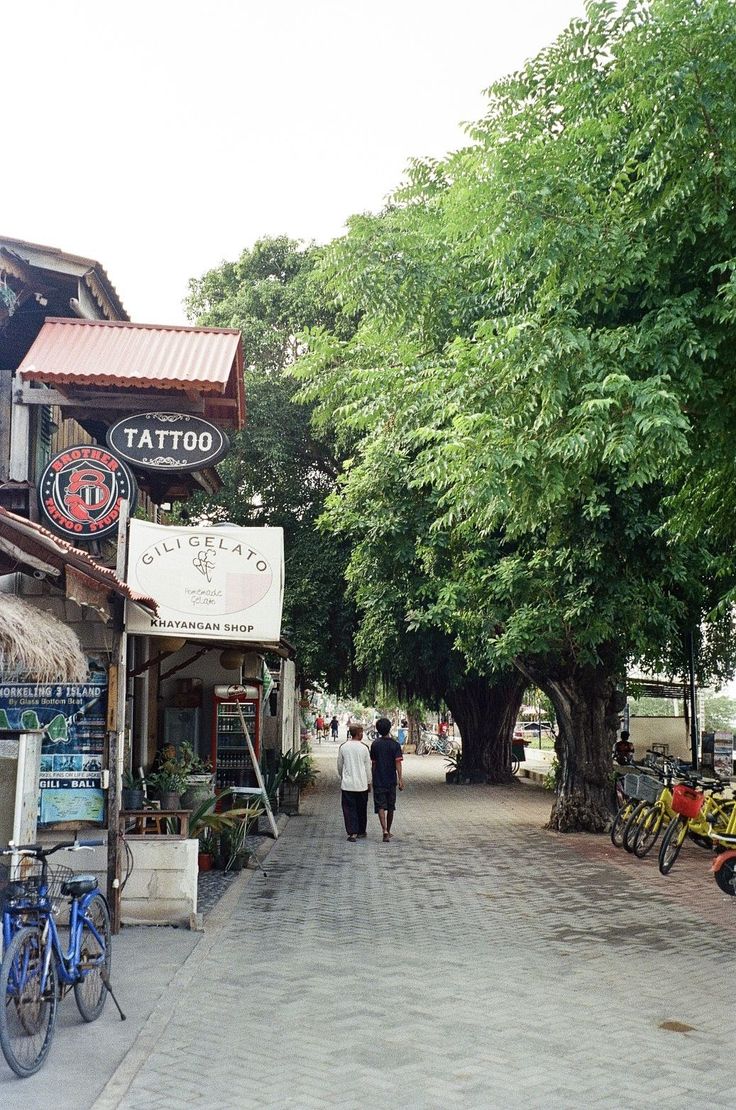 two people walking down the street in front of shops and bicycles parked on the sidewalk