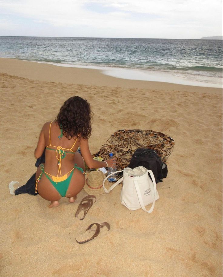 a woman sitting on top of a sandy beach next to a bag and shoelace