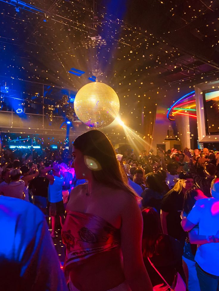 a woman standing in front of a disco ball at a party with other people watching