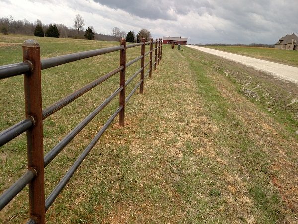 a long fence in the middle of a grassy field with a barn in the distance