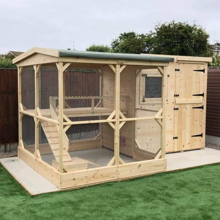 a large wooden chicken coop with doors open on top of grass covered ground next to a fence