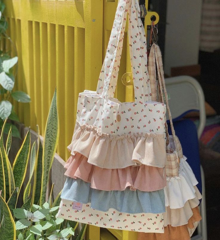 a multicolored purse hanging on a yellow fence next to some plants and flowers