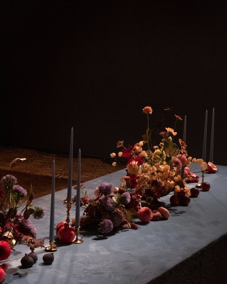 flowers and candles are lined up on a blue table cloth in front of a black background