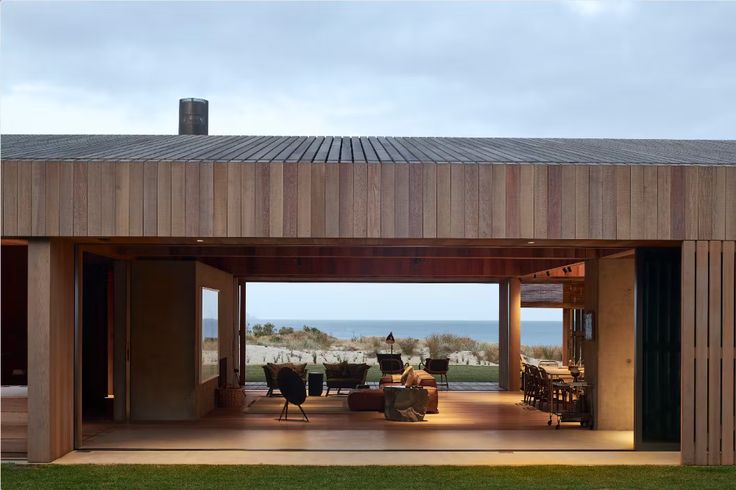 an open living area with chairs and tables on the ground next to the ocean at dusk