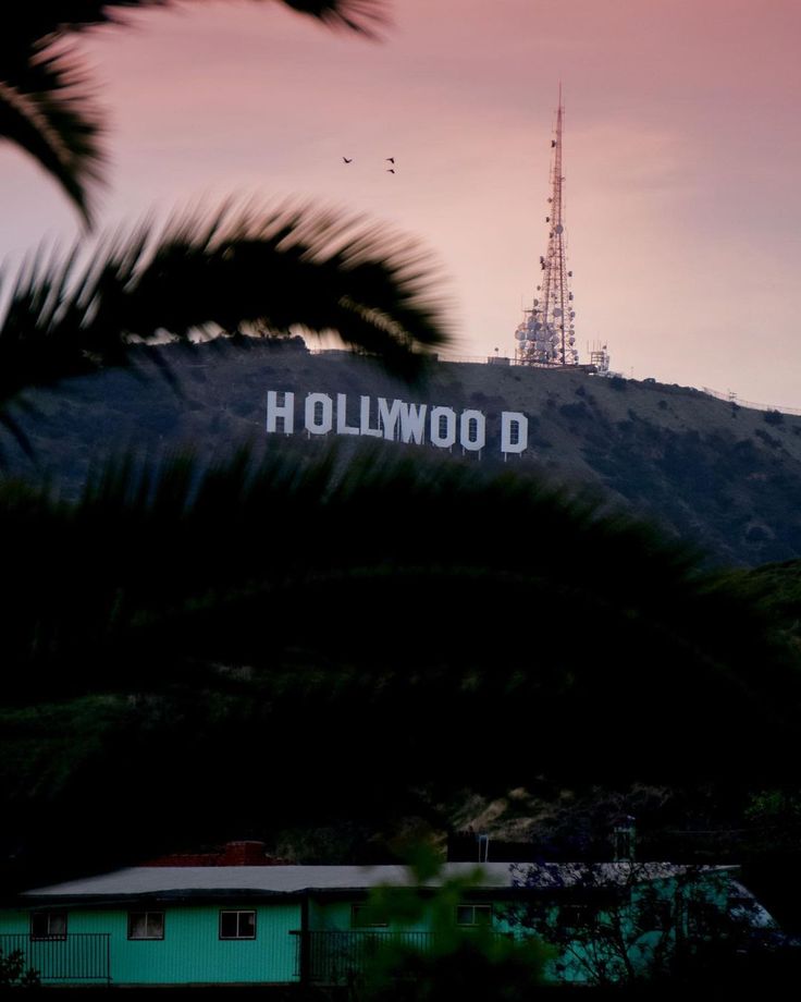 the hollywood sign is seen through palm trees in front of a building with a radio tower on top