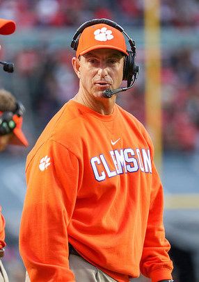 an orange and white football coach wearing headphones on the sidelines with his team