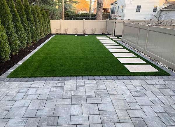 a backyard with grass and white stepping stones on the ground in front of a fence