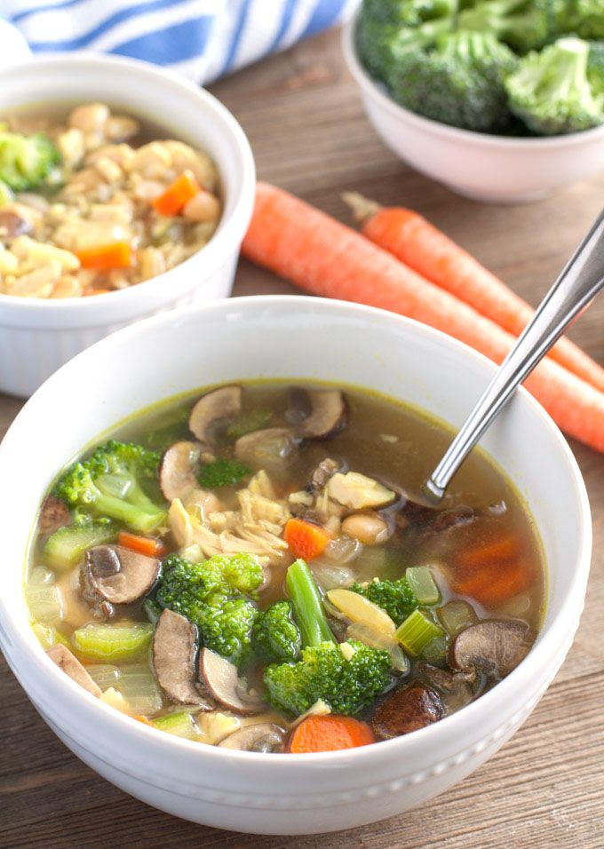 two bowls of soup with carrots, broccoli and other vegetables on a table