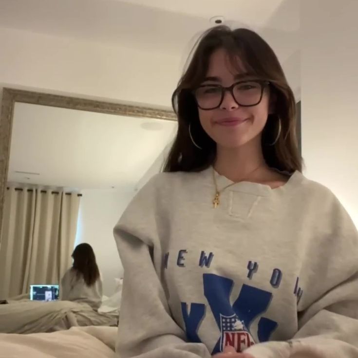 a woman wearing glasses standing in front of a mirror with her arms crossed and looking at the camera