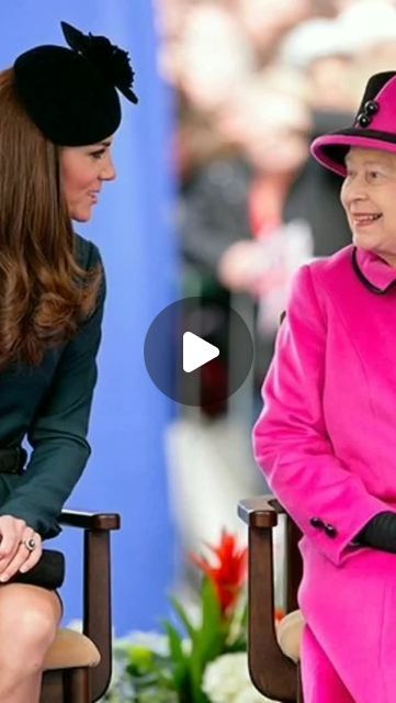 the queen is talking to an older woman in a pink suit and black hat while she sits on a chair