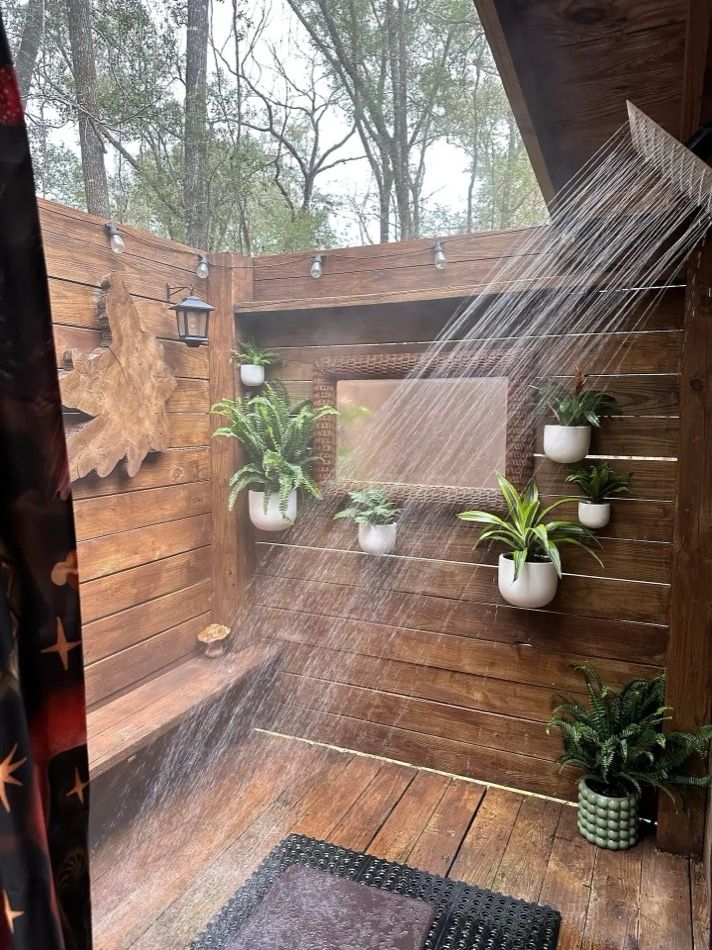 a shower head is sprinkled with water in a wooden outdoor shower area surrounded by potted plants