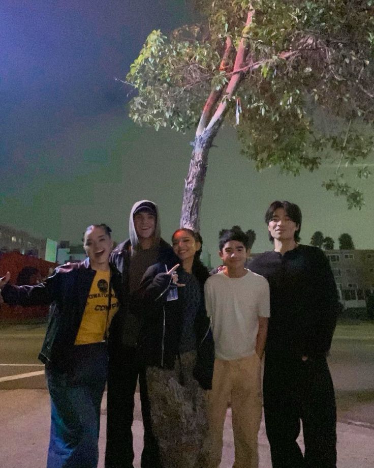 four young men standing next to each other under a tree at night with their arms in the air