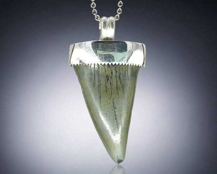 a piece of green glass with a silver chain on a gray background, it looks like something from the past