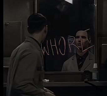 two men standing in front of a mirror with graffiti on it's face and one man has his head turned to the side