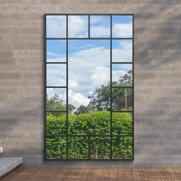 a large mirror sitting on top of a wooden floor next to a window filled with plants