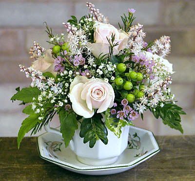 a white flower arrangement in a teacup on a saucer sitting on a table