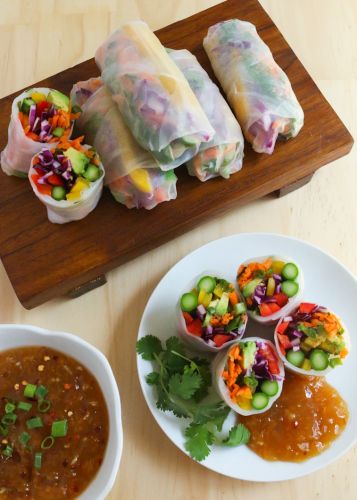 some food is laying out on a wooden board next to bowls of soup and dipping sauce