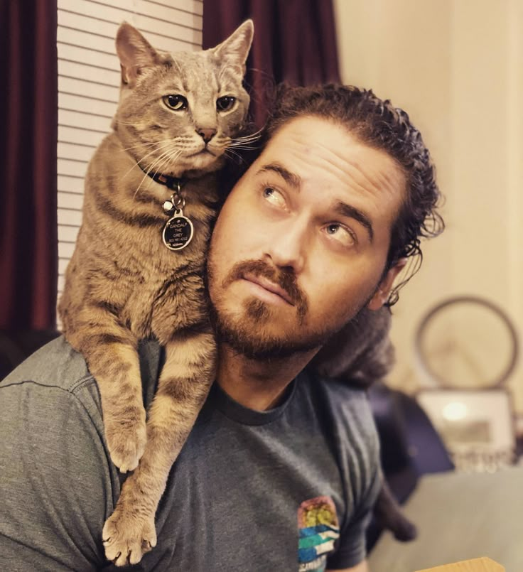 a man is holding a cat on his shoulders and looking up at the camera with an intense look