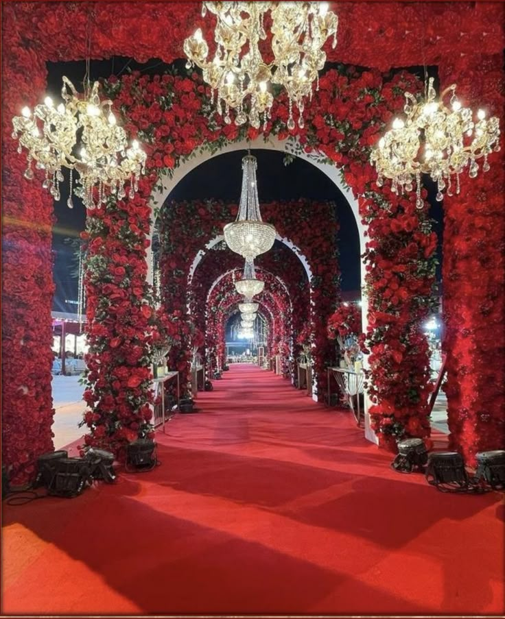 a red carpeted walkway with chandeliers and roses on the walls at night