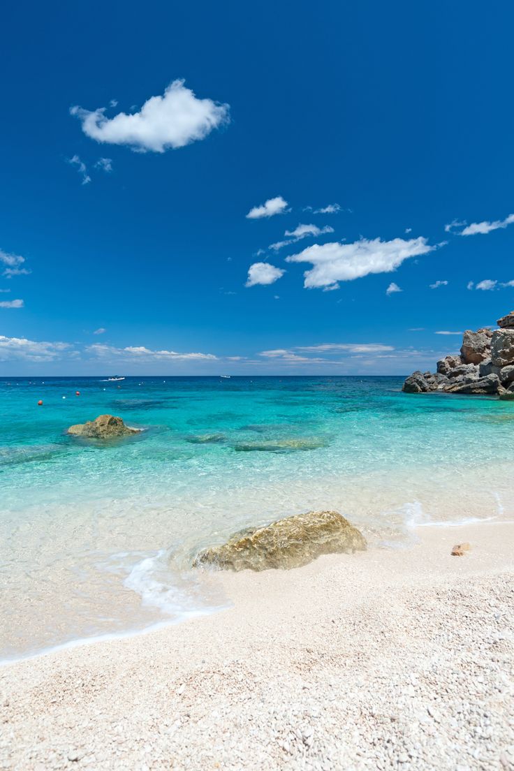 the water is crystal blue and clear with white sand on the beach near some rocks