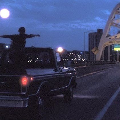 a man standing on the back of a truck in front of a bridge at night