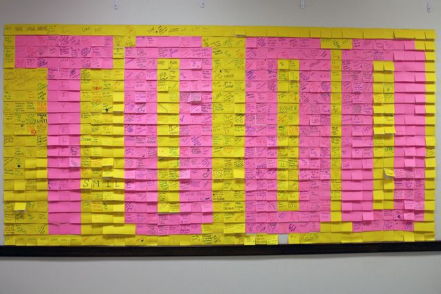 a bulletin board covered in pink and yellow post - it notes on a white wall