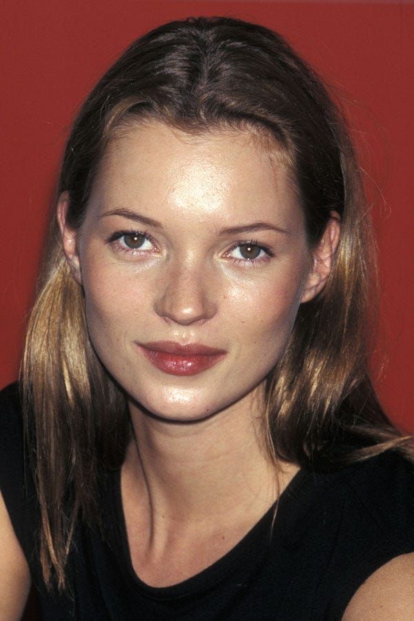 a woman with long hair and blue eyes posing for a photo in front of a red wall